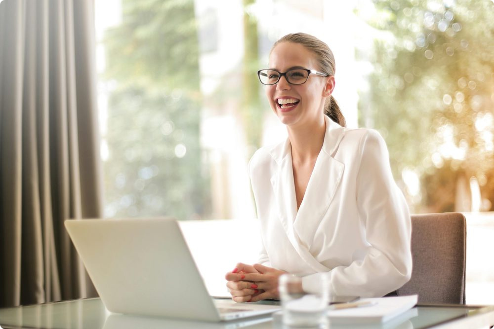 Businesswoman laughing while working on a laptop in a bright office, representing easy-to-use HR compliance software for Australian businesses