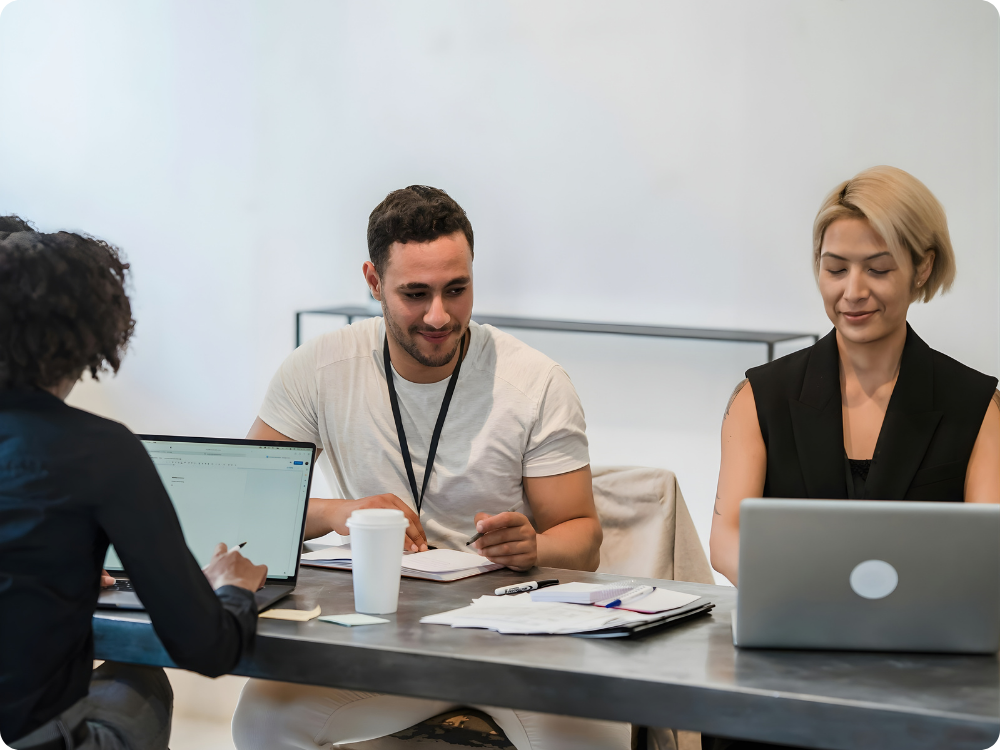 Small startup team working together at a shared desk with laptops, representing lawyer-backed HR with contracts, policies and documents in one platform