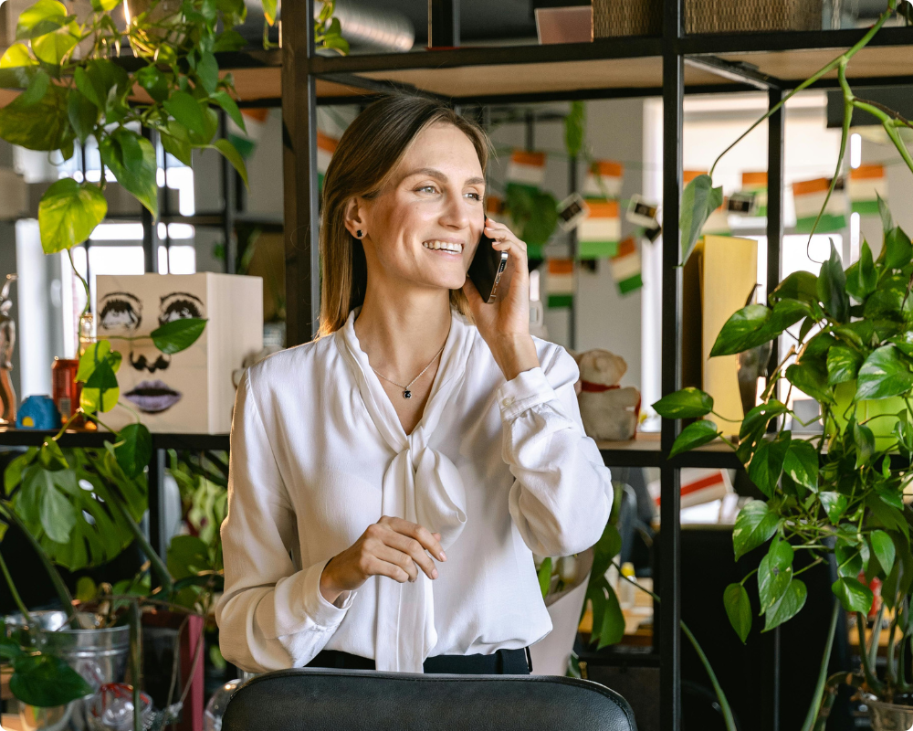 Businesswoman smiling on a phone call in a plant-filled office, representing HR Command's workplace advice line with access to employment lawyers